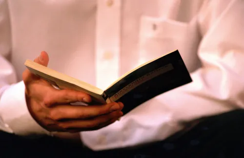 Hand mit einem Buch vor weißem Hemd