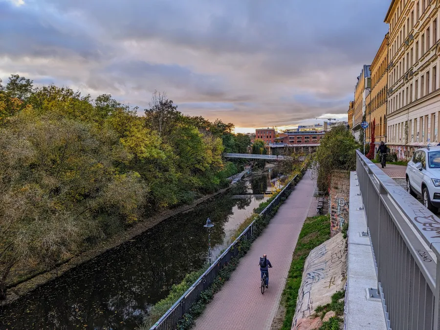 Am Karl-Heine-Kanal in Leipzig, rechts Häuserfassaden, mittig unten ein Radfahrer auf dem Radweg des Kanals, im Hintergrund das Stelzenhaus